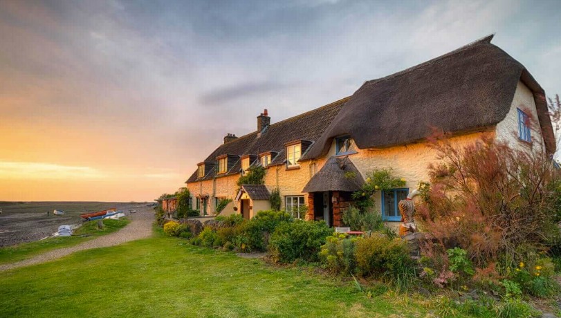 Thatched stone cottages at golden hour with cottage gardens and moored boats beyond